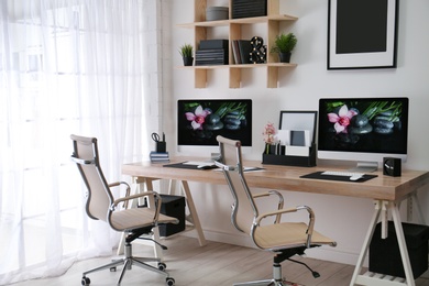 Photo of Modern workplace with large desk and computers in room. Stylish interior