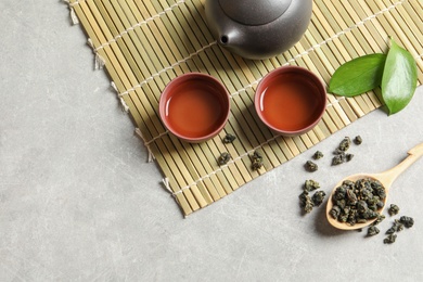 Composition with spoon of Tie Guan Yin Oolong tea and brewed beverage on grey table, top view. Space for text