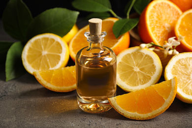 Photo of Bottle of essential oil and citrus fruits on grey table