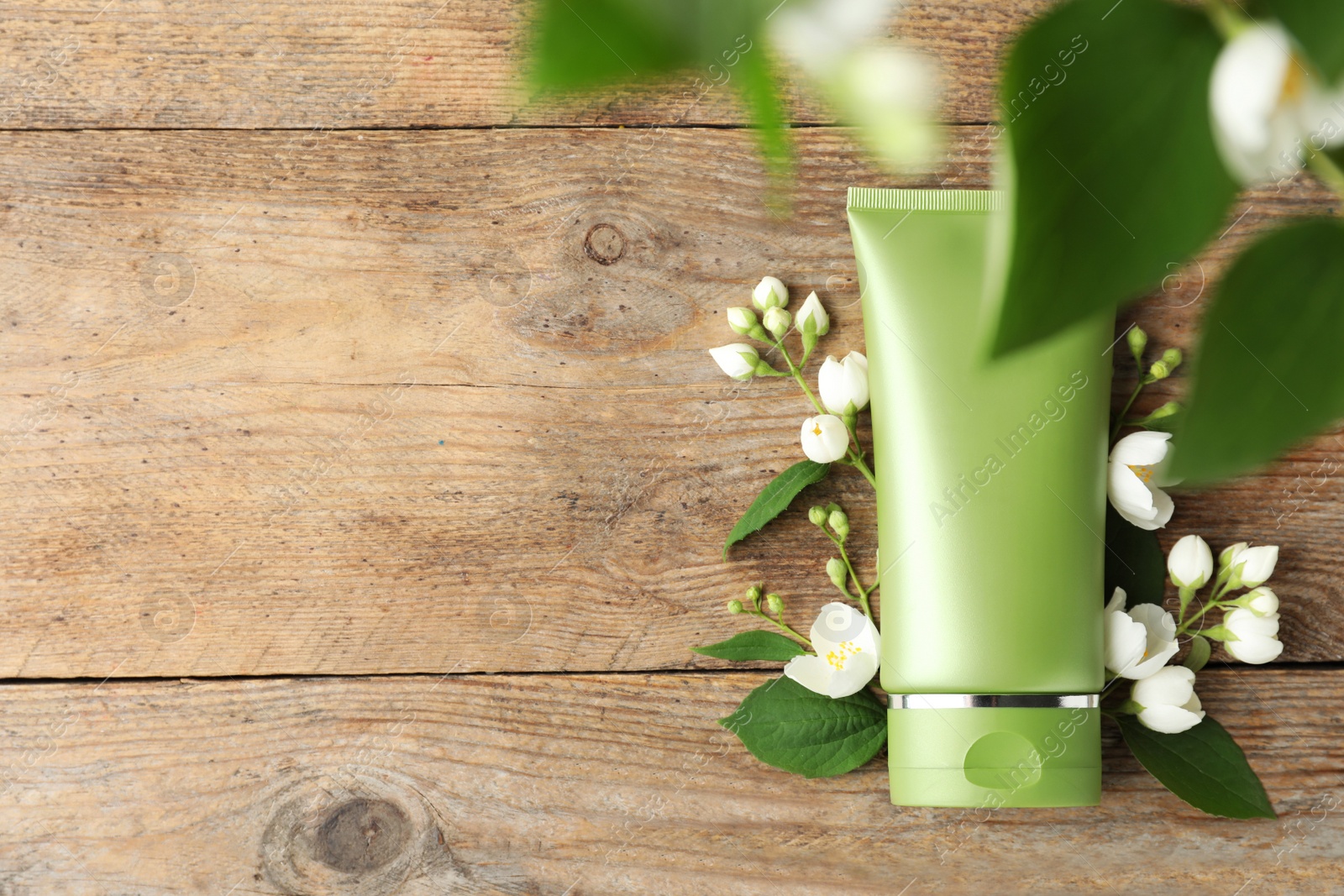 Photo of Tube of cosmetic product and flowers on wooden table, flat lay. Space for text