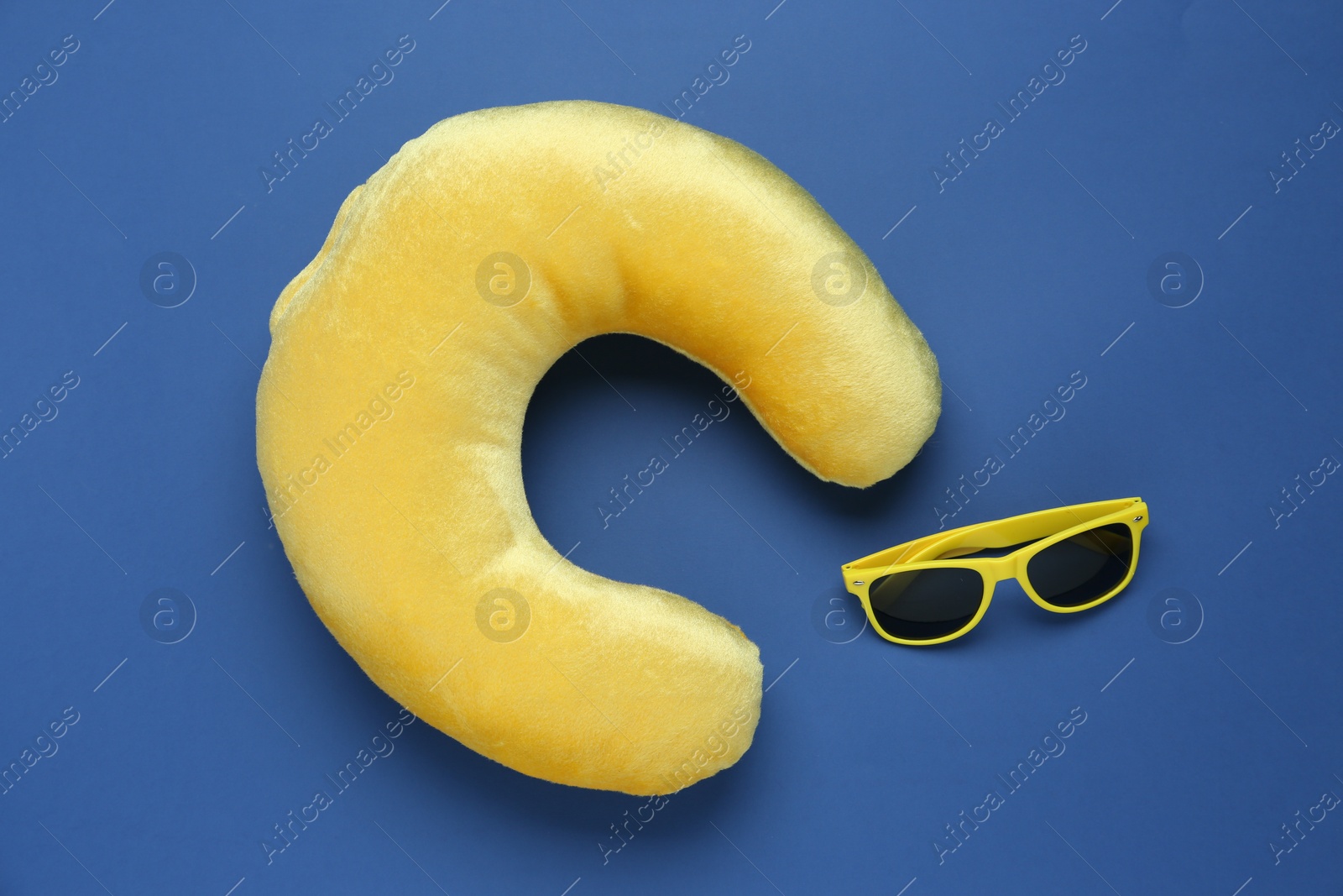 Photo of Yellow travel pillow and sunglasses on blue background, flat lay