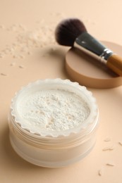 Photo of Rice loose face powder and makeup brush on beige background, closeup