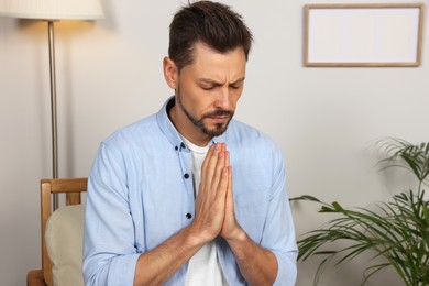 Photo of Man with clasped hands praying in room at home