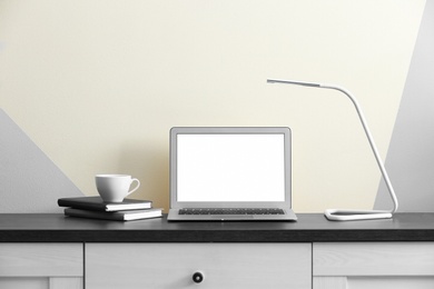 Modern laptop on desk near color wall, space for design. Home workplace