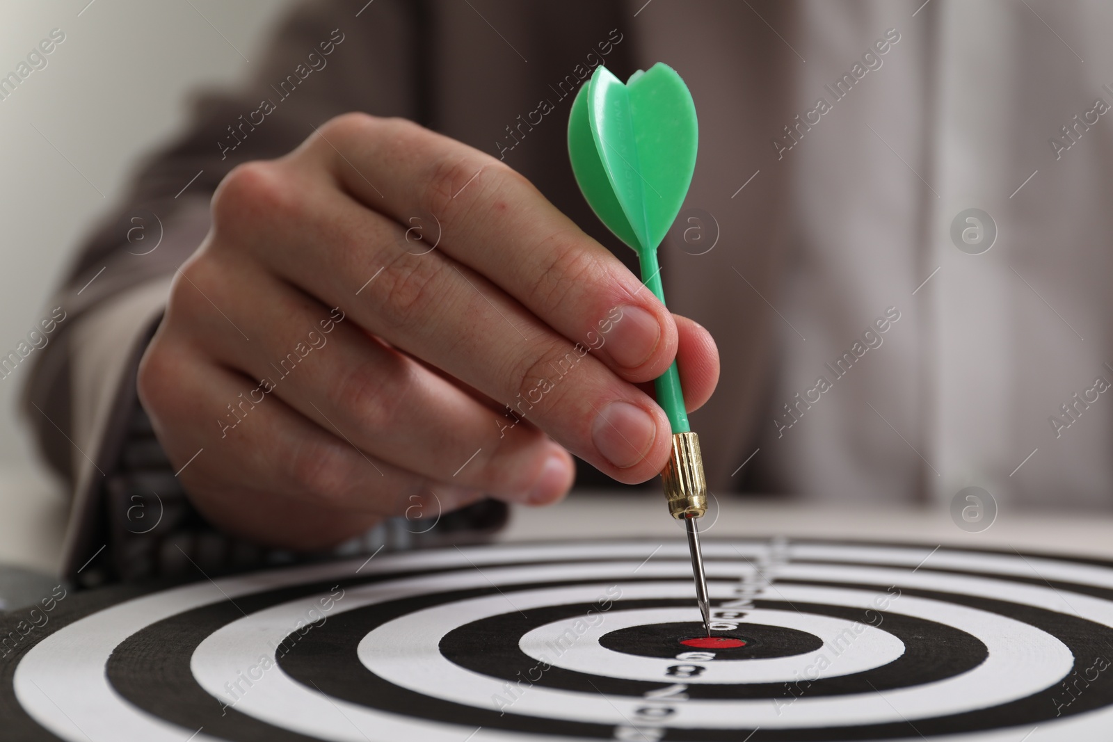 Photo of Business targeting concept. Man with dart aiming at dartboard at table, closeup