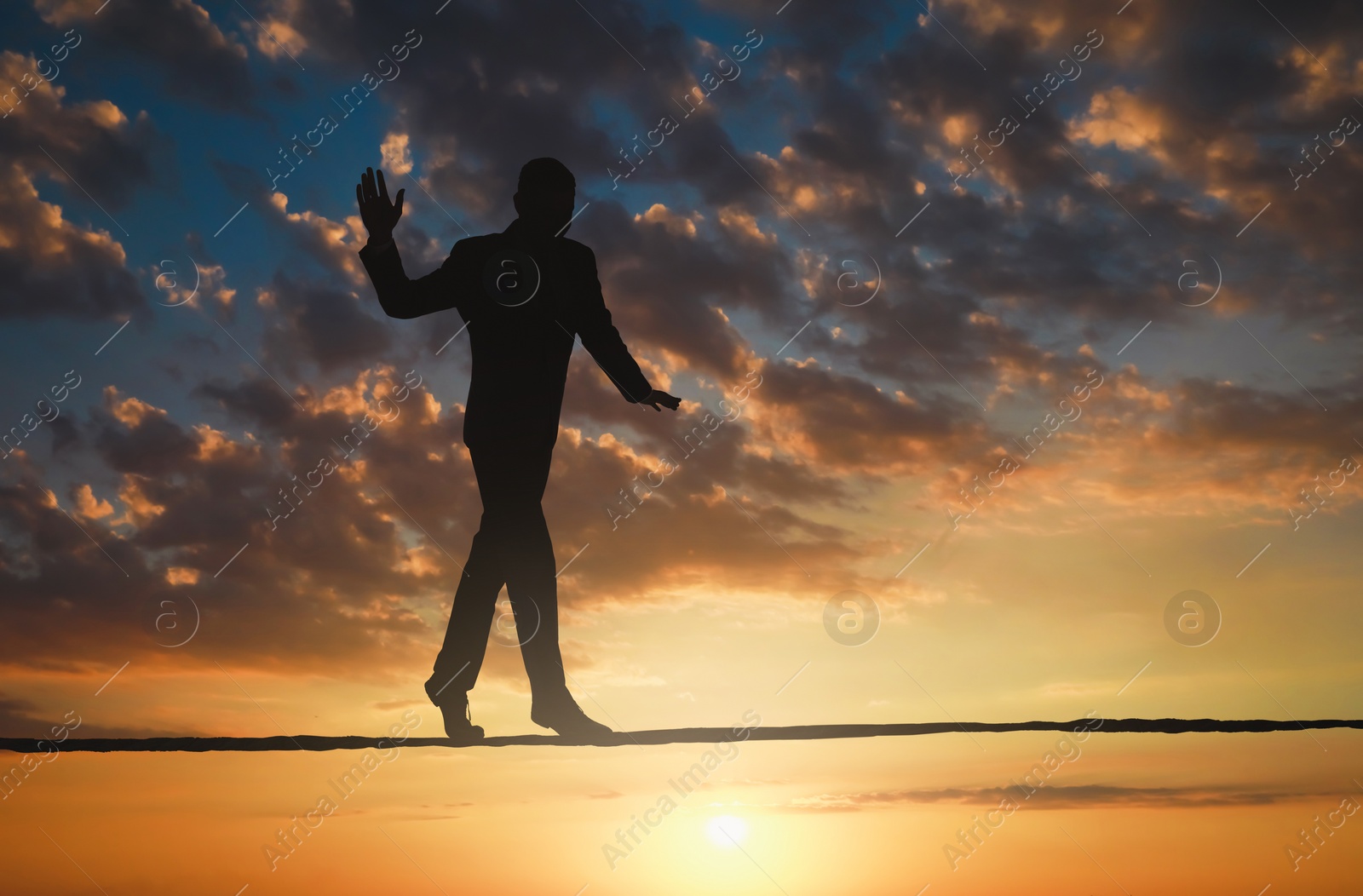 Image of Risks and challenges of owning business. Silhouette of man balancing on rope in sunset sky