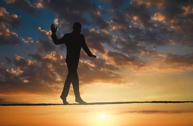 Image of Risks and challenges of owning business. Silhouette of man balancing on rope in sunset sky