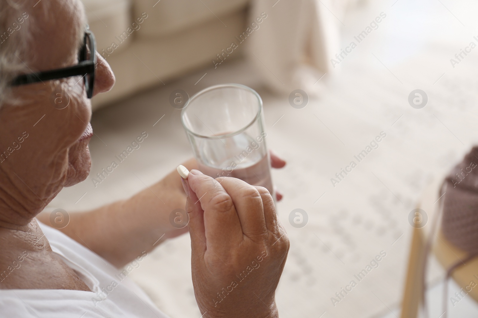 Photo of Senior woman with glass of water taking pill at home, closeup