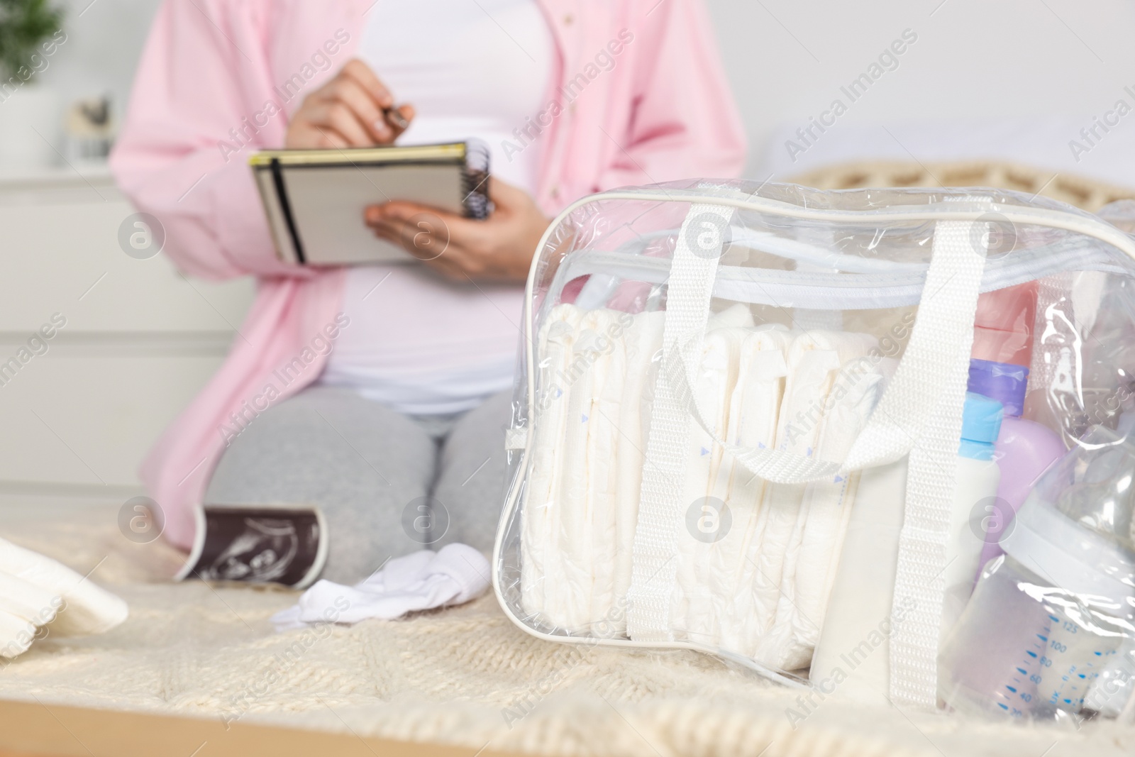 Photo of Pregnant woman preparing list of necessary items to bring into maternity hospital in bedroom, focus on bag