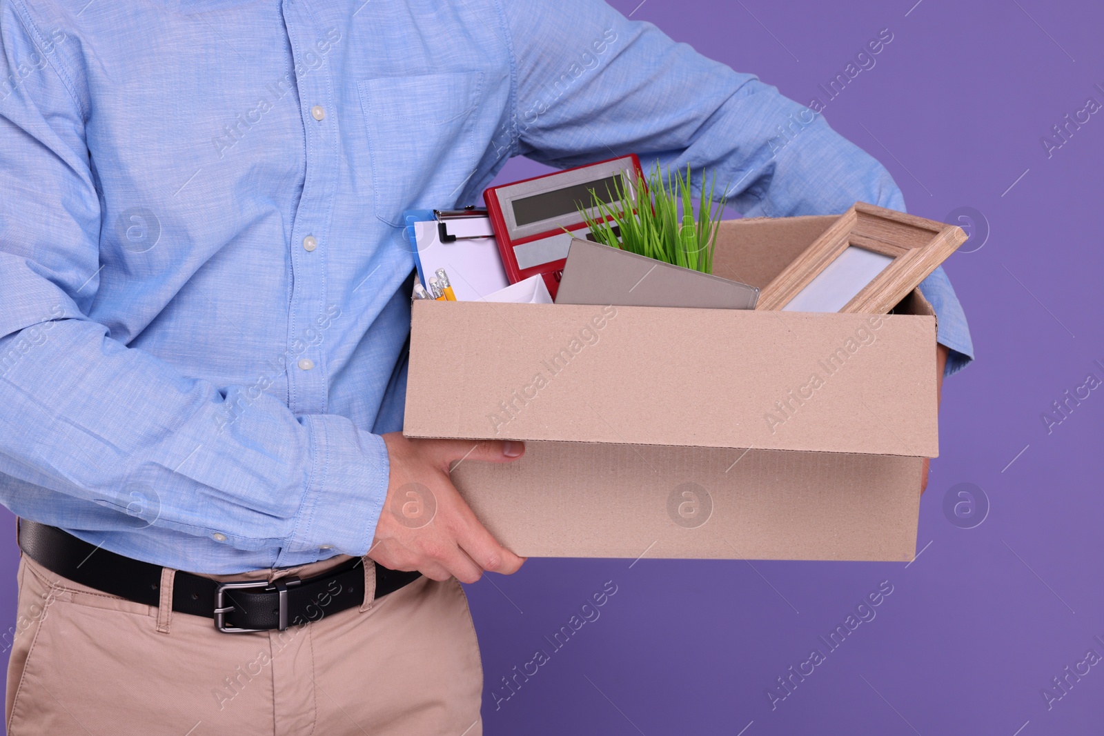 Photo of Unemployed man with box of personal office belongings on purple background, closeup