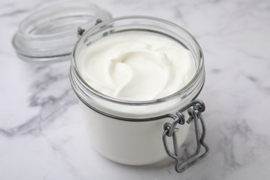 Delicious natural yogurt in glass jar on white marble table, closeup