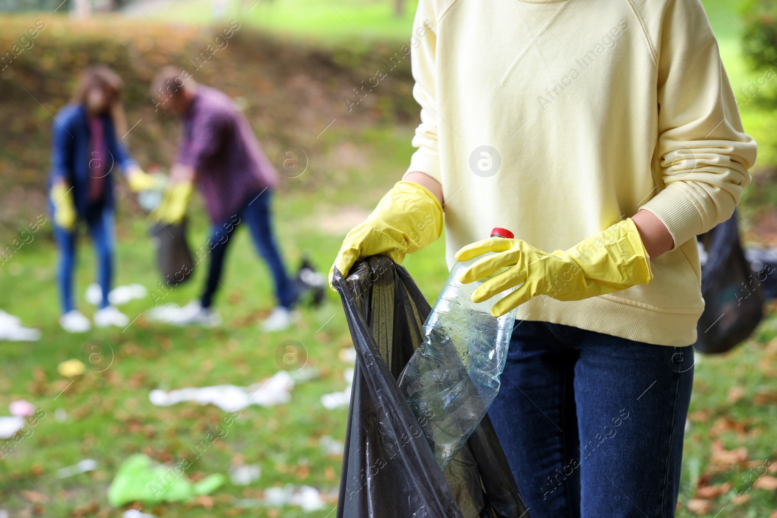 Photo of Woman with plastic bag collecting garbage in park, closeup