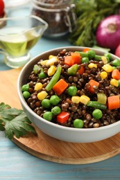 Photo of Delicious lentils with vegetables in bowl and parsley on light blue wooden table, closeup