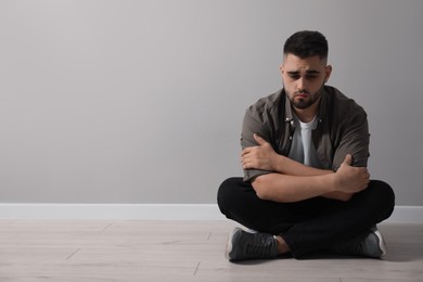 Photo of Sad man sitting on floor near light grey wall. Space for text