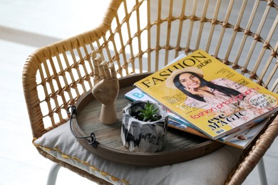 Wooden tray with houseplant and magazines on chair indoors