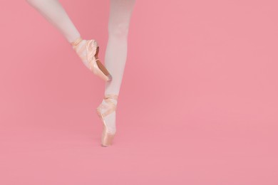 Photo of Young ballerina in pointe shoes practicing dance moves on pink background, closeup. Space for text