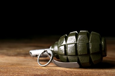 Photo of Hand grenade on wooden table against black background, closeup. Space for text