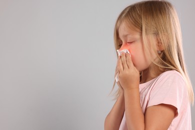 Suffering from allergy. Little girl with tissue sneezing on light gray background, space for text