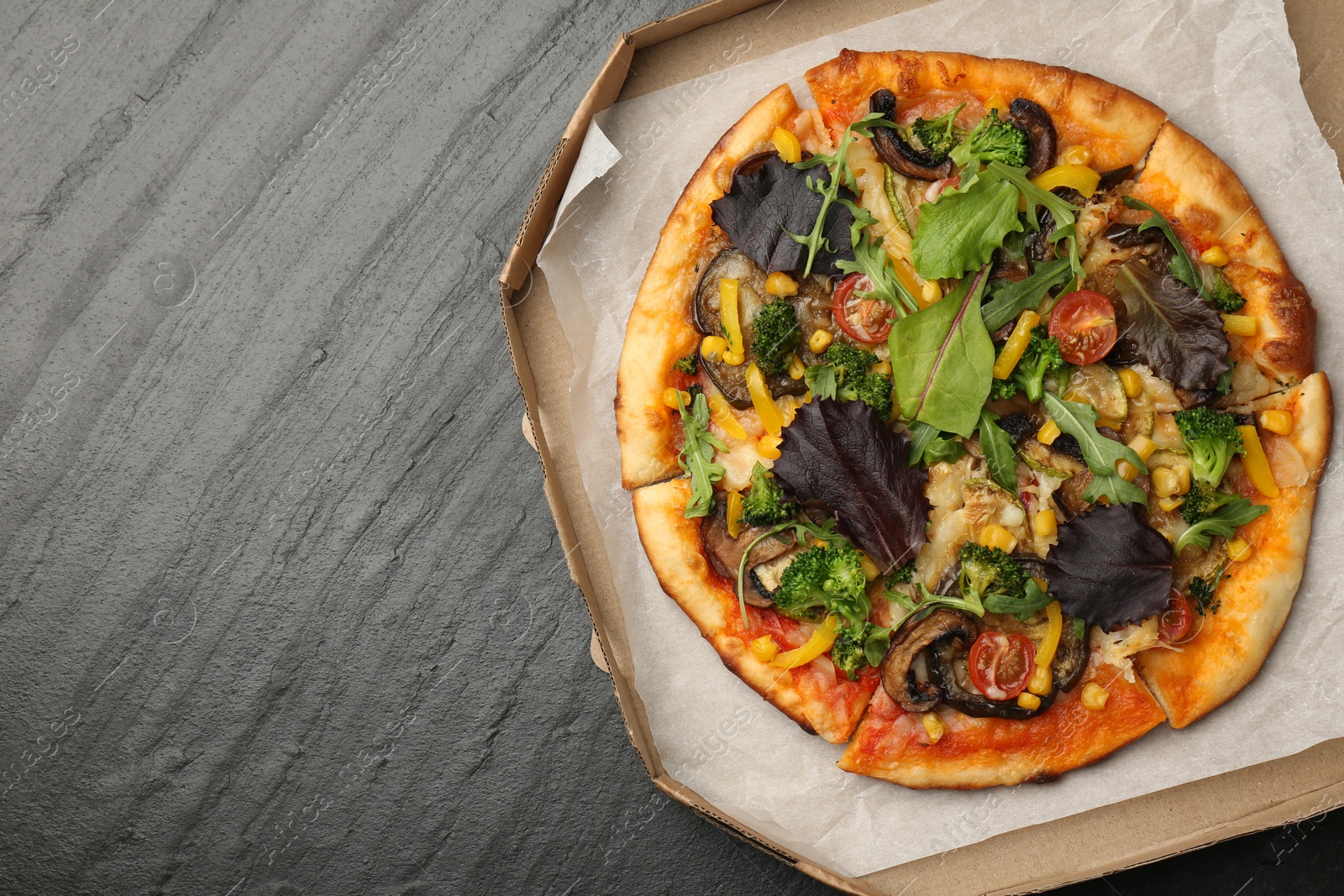 Photo of Delicious vegetarian pizza with mushrooms, vegetables and greens in box on black table, top view. Space for text