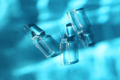 Skincare ampoules in sunlight on light blue background, top view