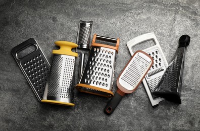 Different modern graters on grey table, flat lay