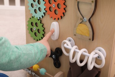 Photo of Little child playing with busy board indoors, closeup