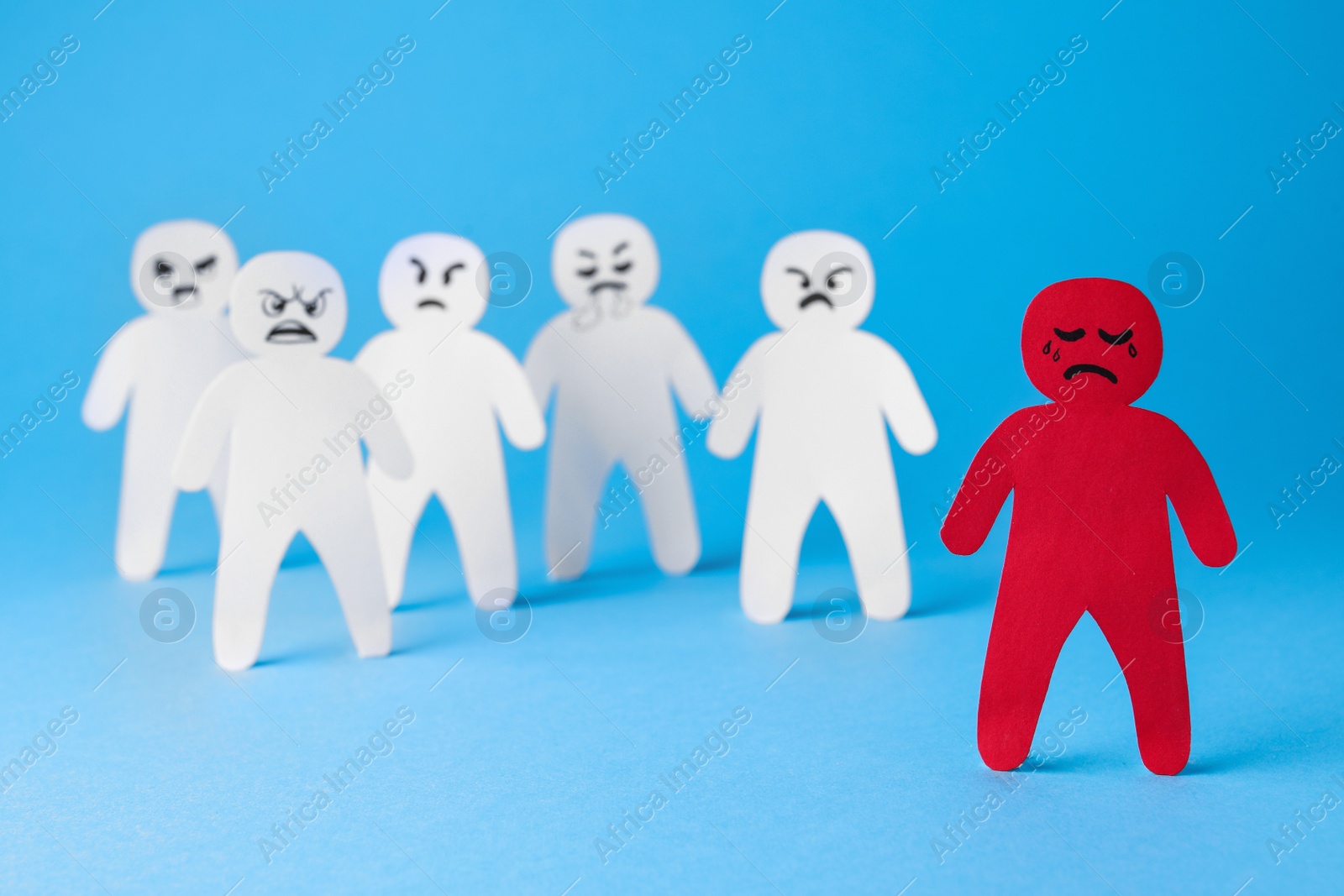 Photo of White paper figures and one red on light blue background. Bullying concept