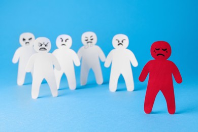 Photo of White paper figures and one red on light blue background. Bullying concept