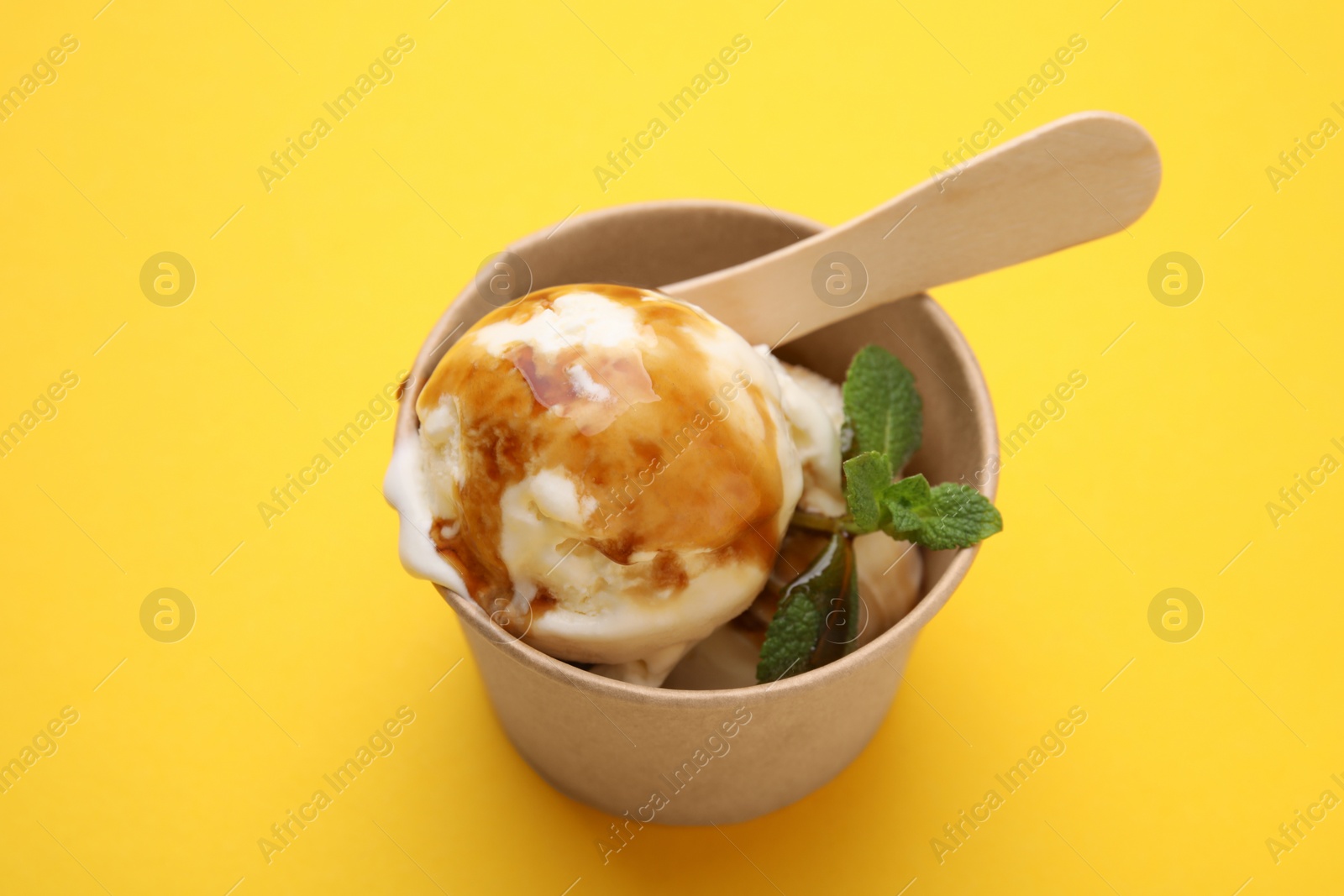 Photo of Scoops of ice cream with caramel sauce and mint leaves on yellow table, above view