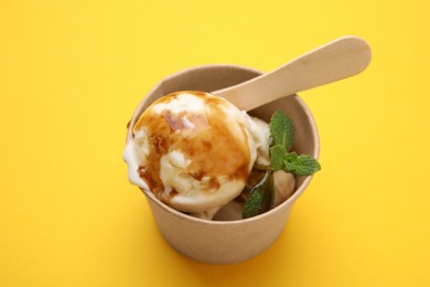 Photo of Scoopsice cream with caramel sauce and mint leaves on yellow table, above view