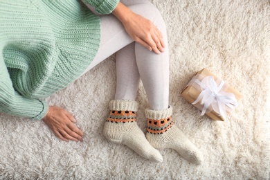 Photo of Woman wearing knitted socks on rug, top view. Warm clothes