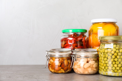 Glass jars with different pickled vegetables on grey table. Space for text