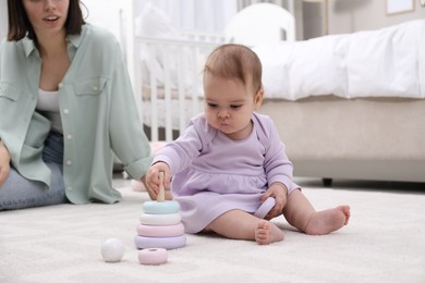 Photo of Cute baby girl playing with toy pyramid near mother on floor at home