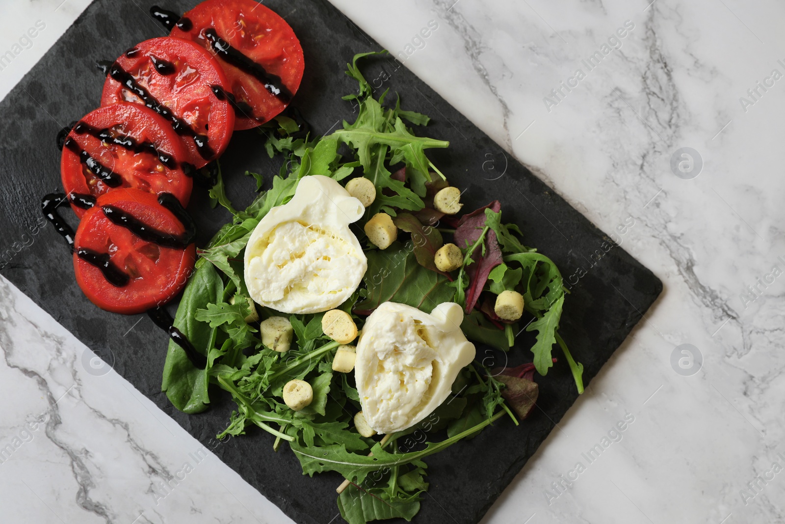 Photo of Delicious burrata cheese, tomatoes and arugula on white marble table, top view