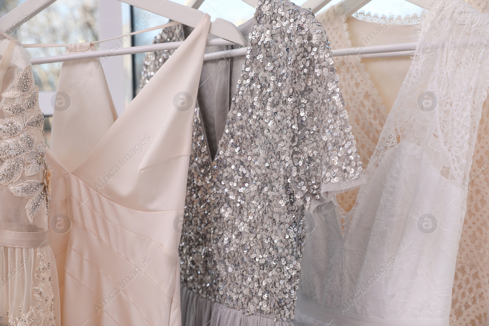 Photo of Hangers with different beautiful dresses in atelier, closeup