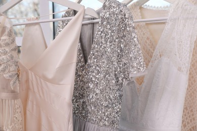 Photo of Hangers with different beautiful dresses in atelier, closeup