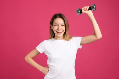 Photo of Woman with dumbbell as symbol of girl power on pink background. 8 March concept