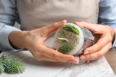 Photo of Woman making conifer candle at table, closeup