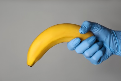 Doctor holding banana symbolizing male sexual organ on grey background, closeup. Potency problem