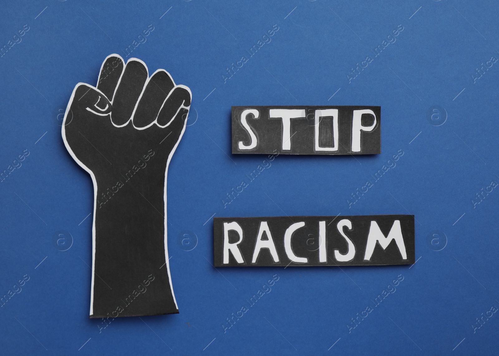 Photo of Words Stop Racism near paper hand with clenched fist on blue background, flat lay