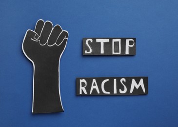 Photo of Words Stop Racism near paper hand with clenched fist on blue background, flat lay