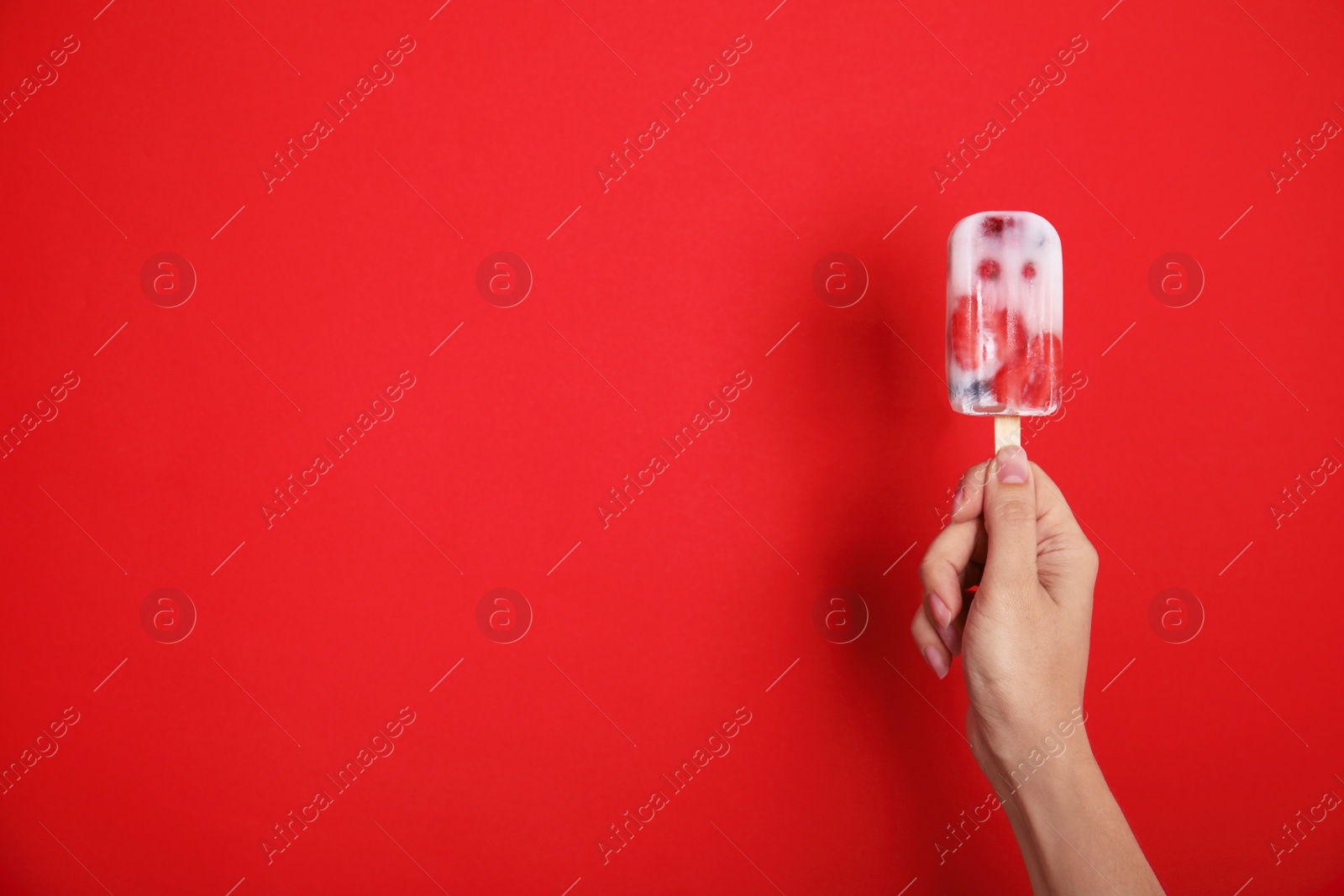 Photo of Woman holding berry popsicle on red background, closeup. Space for text