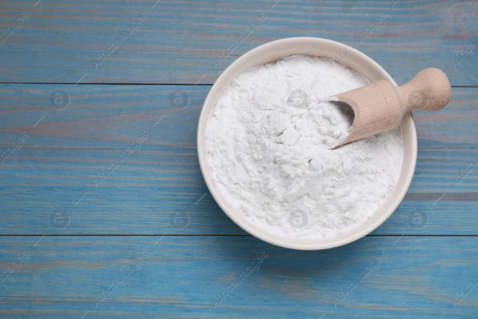 Photo of Bowl and scoop of natural starch on light blue wooden table, top view. Space for text