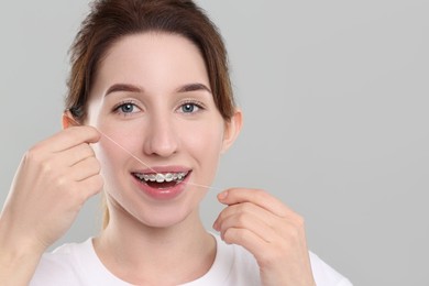 Photo of Smiling woman with braces cleaning teeth using dental floss on grey background