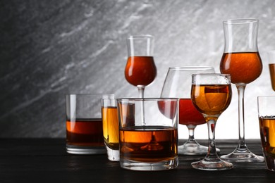 Different delicious liqueurs in glasses on dark wooden table