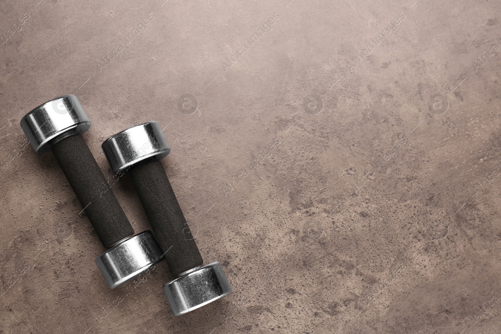 Photo of Metal dumbbells on brown textured table, flat lay. Space for text