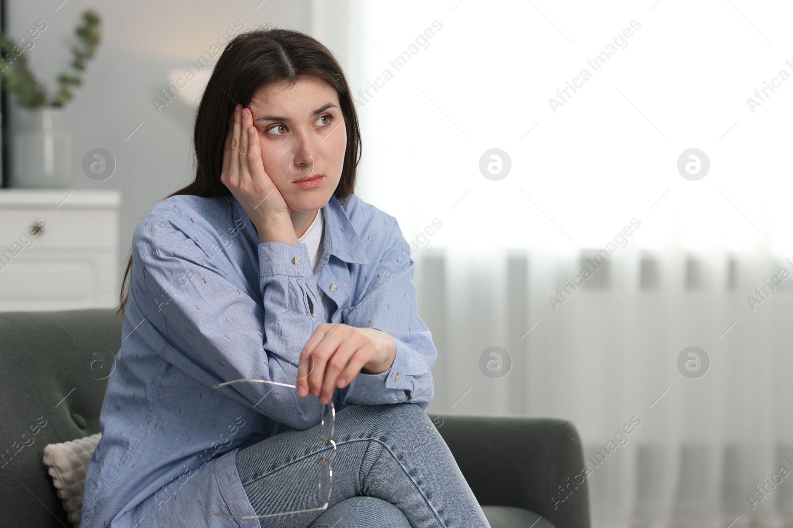 Photo of Overwhelmed woman with glasses sitting on sofa at home. Space for text