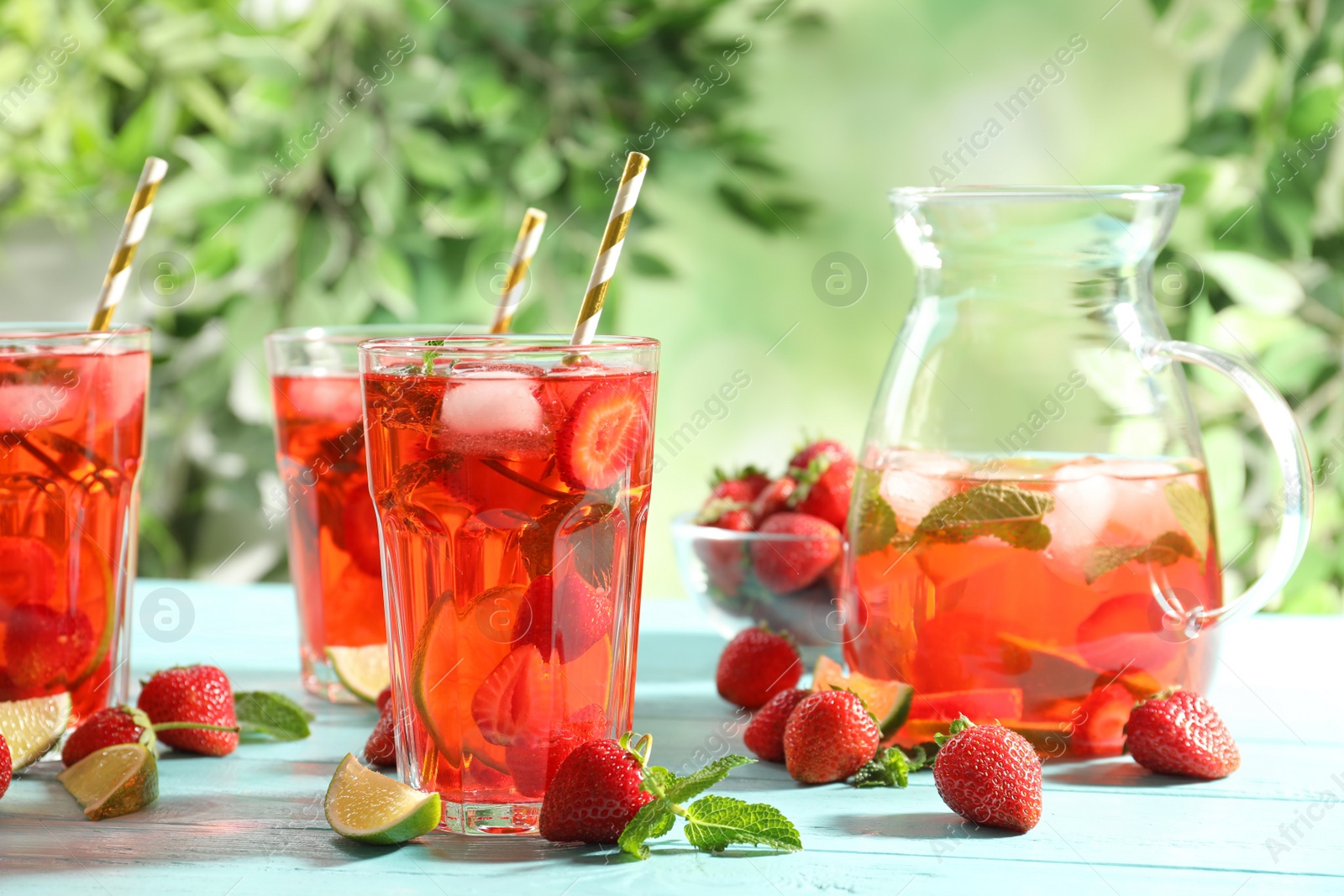 Photo of Refreshing drink with strawberry and lime on light blue wooden table