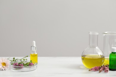 Cosmetic oil, laboratory dishware and flowers on white table, space for text