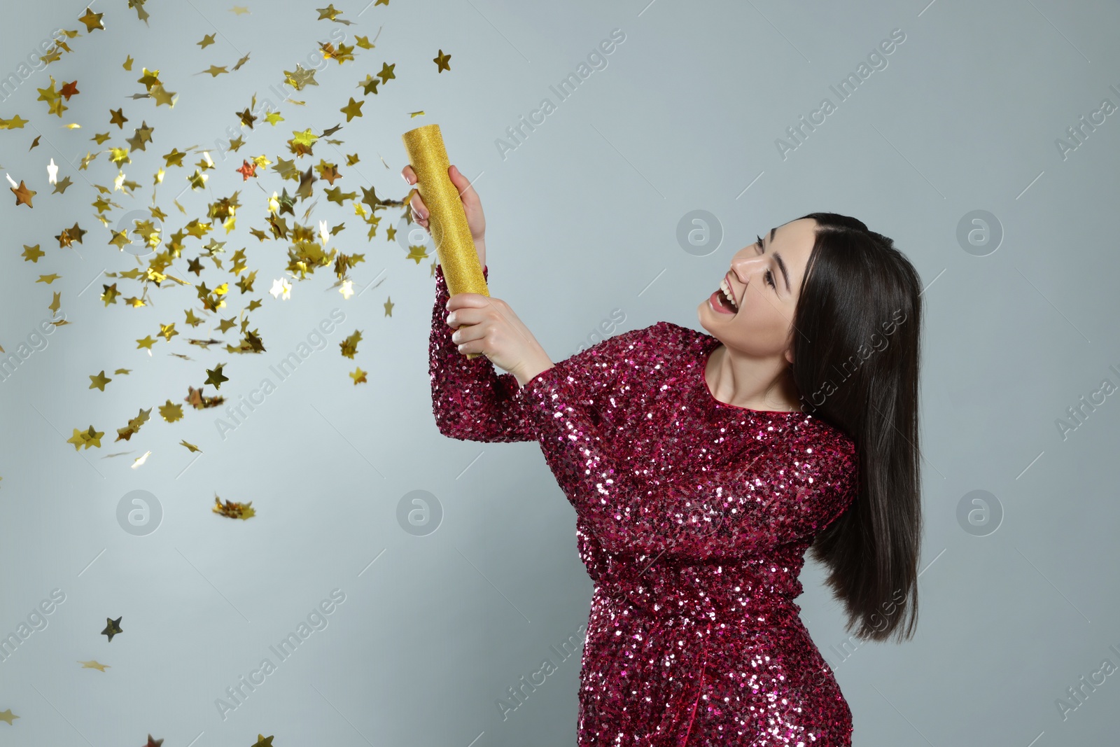 Photo of Young woman blowing up party popper on light grey background